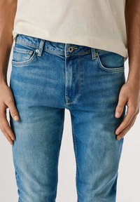 Jasnoniebieskie dżinsy o slim fit, z pięcioma kieszeniami, zapinane na zamek oraz z delikatnym przetarciem na udach.