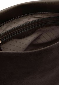 Interno di una borsa in camoscio marrone con tasca con cerniera. Foderato con un tessuto a motivo con sottili strisce e dettagli logo.