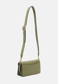 Oliwkowa skórzana torebka na ramię z regulowanym paskiem, złotymi elementami metalowymi i detalem kieszeni z przodu, zawieszona na tle białym.