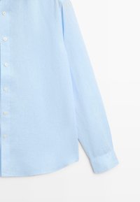 Light blue long-sleeve button-up shirt made of textured fabric, shown from mid-torso to cuff on white background.