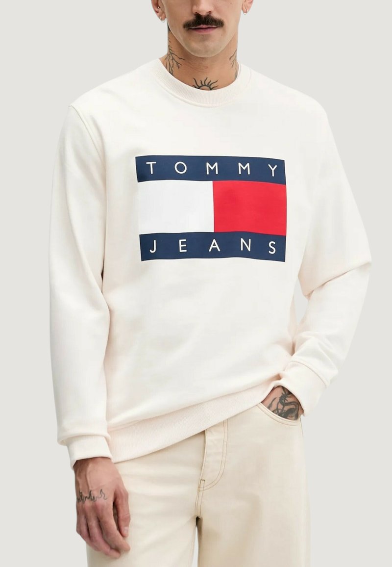 Krämfärgad sweatshirt med en rektangulär grafik som visar texten "TOMMY JEANS", blå och röda accenter samt ribbade muddar och fåll.