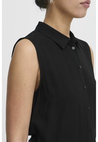 Blusa nera senza maniche con chiusura a bottoni, colletto a punta e tessuto liscio. Presenta una vestibilità rilassata e dettagli di cucitura discreti.