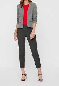 Grå blazer med en tæt pasform, parret med en rød T-shirt og mørke stribede bukser. Outfittet suppleres af sorte hæle-sandaler.