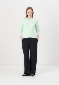 Pull en maille côtelée vert clair avec un col rond, associé à un pantalon large taille haute bleu marine foncé. Chaussures noires minimalistes.