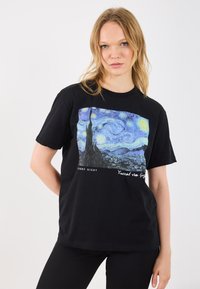 T-Shirt preta de algodão com uma vibrante representa�ção impressa de "Noite Estrelada" de Vincent van Gogh, apresentando cenas detalhadas e texto na parte inferior.