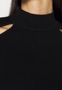 Zwarte geribbelde gebreide top met een hoge kraag en een uitgesneden schouderdetail, met een textuurstof en een aansluitende pasvorm.