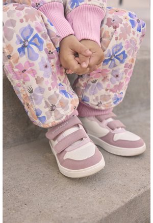 Rosa Hose mit Blumenmuster, elastische Bündchen und rosa Pulloverärmel. Hellrosa und weiße Sneaker mit Klettverschlüssen und strukturierten Akzenten.