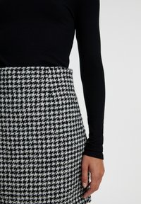 Zwarte geribbelde langemouwtop gecombineerd met een gestructureerde zwart-wit houndstooth rok, die onderscheidende patronen en een op maat gemaakte pasvorm toont.