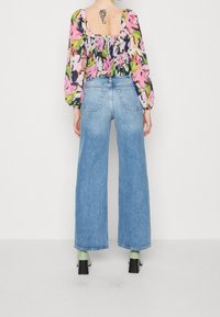 Väljer en blommig blus med puffärmar i rosa, gröna och blå nyanser, som matchas med vida ljusblå jeans och svarta klackskor.