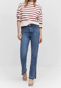 Pull rayé blanc et rouge, ample, associé à un jean bleu taille haute avec un ourlet effiloché et des fentes latérales, complété par des sandales blanches.