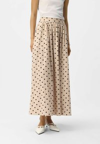 Falda larga, beige, con lunares negros. Presenta una cintura fruncida y una silueta fluida, confeccionada con un tejido suave. Combinada con zapatos blancos.