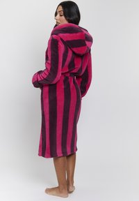 Bata con capucha de textura suave que presenta amplias franjas verticales en rosa brillante y púrpura oscuro, con un dobladillo hasta la rodilla y cinturilla atada.