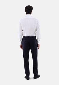 Weißes Langarmhemd mit Manschettenknöpfen, kombiniert mit marineblauen Hosen und schwarzen Schuhen. Das Hemd hat einen klassischen Kragen und eine glatte Textur.
