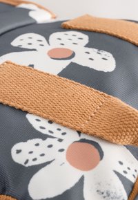 Floral design fabric with gray background, featuring white flowers, orange center, and tan textured straps. Close-up of material and stitching.