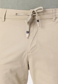 Beige shorts i et tekstureret stof med en snøre i taljen, der har tofarvede ender og en sidelomme. Enkle, afslappede design.