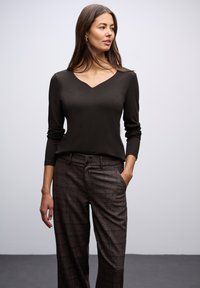 Tmavě hnědý dlouhý rukáv top s výstřihem do V, spárovaný s kostkovanými širokými kalhotami v odstínech hnědé a šedé, se zapínáním na knoflík.