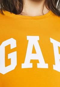 Camiseta de algodón amarilla con letras en bloque blancas que dicen "GAP". Diseño de cuello redondo con textura suave y sin patrones adicionales.