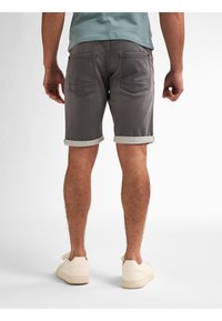Shorts de mezclilla gris con dobladillos enrollados, dos bolsillos traseros y un diseño ajustado, combinados con zapatillas de color crema.