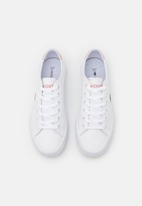 Hvite sneakers med en glatt syntetisk overdel, snørebånd foran og lys rosa detaljer på hælen. Gummisåle med et teksturert mønster.