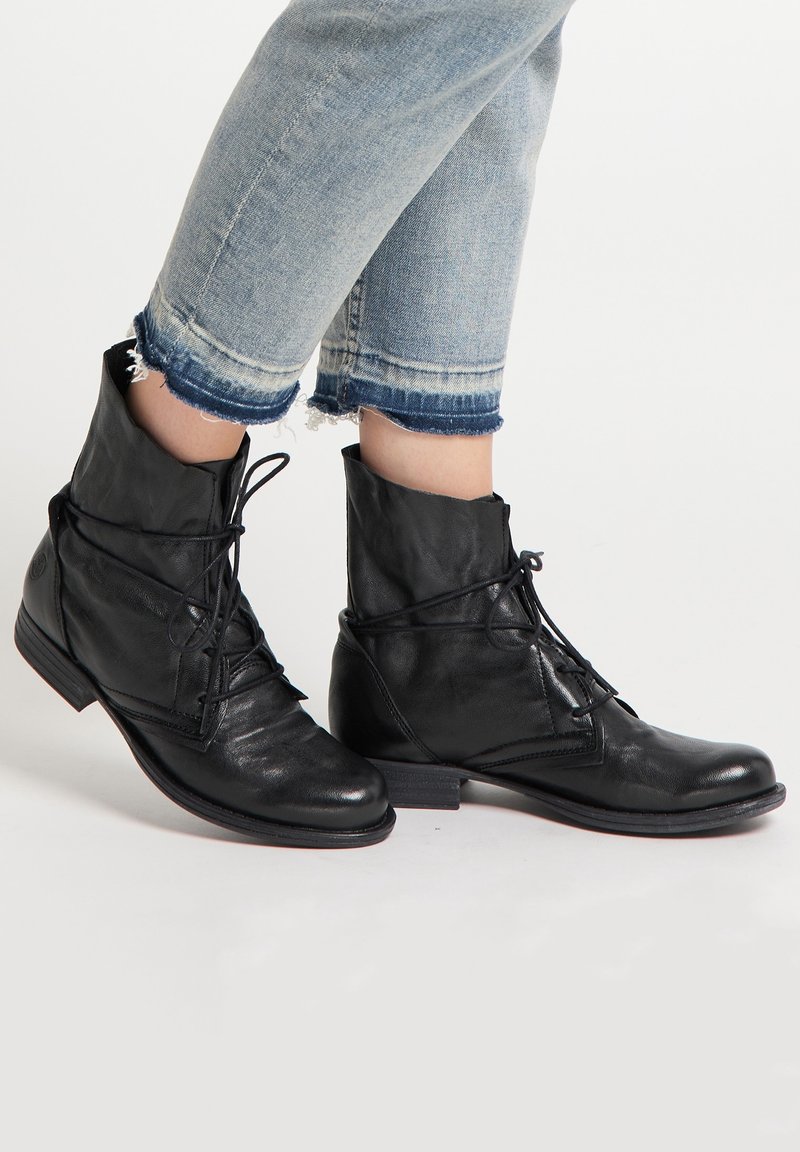 Bottines en cuir noir avec un design à lacets, bouts ronds, talons bas et détails de couture subtils. Portées avec un jean bleu cropped effiloché.