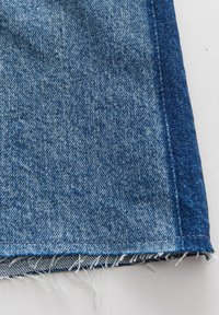 Denimstoff in Hellblau mit einem ausgefransten Saum und dunkleblaue Seitenpanels. Hat eine subtile Textur mit einem Standardnähmuster.