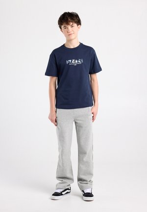 Marineblauw T-shirt met witte grafische print, gecombineerd met lichtgrijze joggingbroek met zijstrepen en zwarte sneakers met witte accenten.