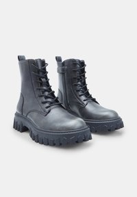 Botine negre din piele cu șireturi în față, fermoar lateral, talpă chunky din cauciuc și detalii texturate pe talpă pentru aderență.