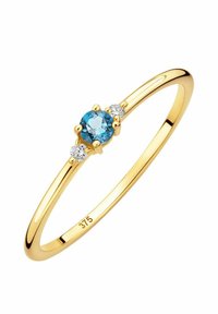 Anello in oro con un centrale pietra rotonda di acquamarina, affiancata da due piccole pietre rotonde trasparenti, con una fascia liscia e lucida.