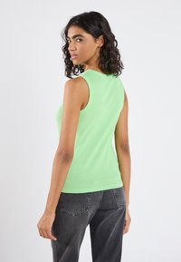 Lys grøn ribbet tanktop med en tætsiddende form, rund halsudskæring og uden ærmer, parret med mørkegrå vidde jeans.