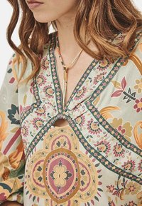 Blusa con estampado floral en colores pastel, que presenta un diseño de escote en V, costuras intrincadas y una abertura central con detalles fruncidos.