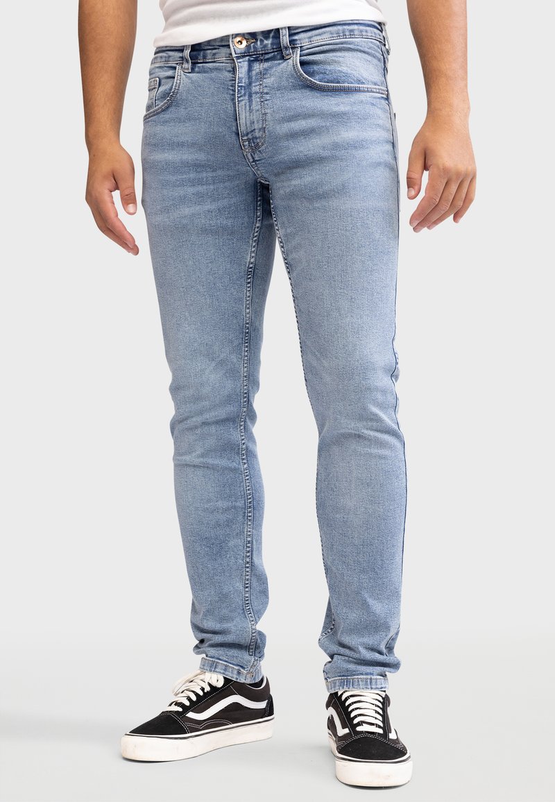 Hellblaue Jeans aus Denim mit schlankem Schnitt, die ein klassisches Fünf-Taschen-Design und dezente Used-Effekte aufweisen. Kombiniert mit schwarzen Sneakers.