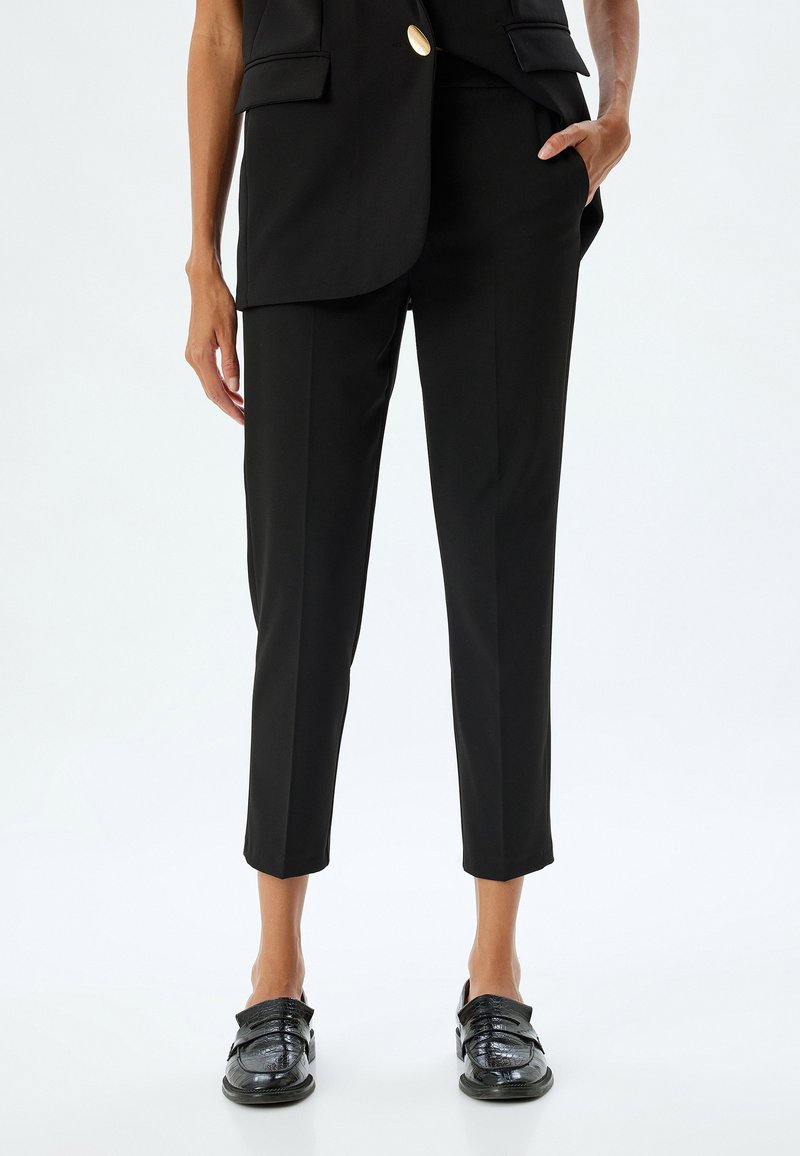 Pantalons noirs ajustés avec une coupe slim, longueur raccourcie et texture lisse. Associés à des chaussures noires brillantes avec un détail de sangle.