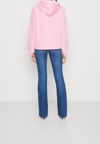 Felpa rosa con cappuccio, dal taglio morbido, abbinata a jeans a zampa d'elefante blu. Il tessuto è morbido, con polsini elastici e un design semplice.