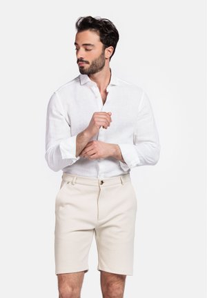 White linen shirt with a relaxed collar, paired with beige shorts featuring a button closure and side pockets. Plain fabric texture.