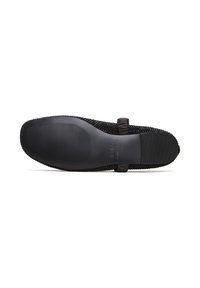 Schwarzer flacher Schuh mit strukturierter Sohle und einer kleinen Schleife, von unten gezeigt, wobei Griffigkeitsdetails und Markenprägung hervorgehoben werden.