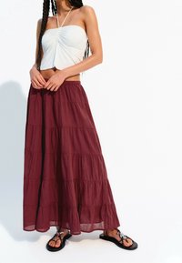 Vit halter crop top matchat med en bordeauxfärgad, lager-på-lager maxi kjol i lätt väv. Sandaler med dekorativa detaljer fullända outfiten.