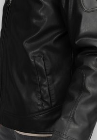 Schwarze Lederjacke mit glatter Textur, Reißverschluss, Seitentasche und geripptem Saum. Verfügt über ein figurbetontes Design und taillierte Ärmel.