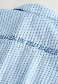 Tissu rayé bleu clair avec le texte "BAKER BY TED BAKER" embossé au centre en lettres bleues assorties.