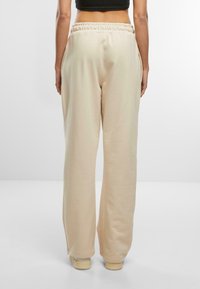 Beige weit geschnittene Jogginghose aus weichem Stoff, mit elastischem Bund und seitlichen Taschen, am Knöchel gesäumt und mit einem glatten Finish.