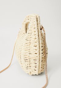 Vevd stråveske i off-white med en rund form, korte håndtak og en avtakbar kjede i gulltone. Teksturert med et flette-mønster.