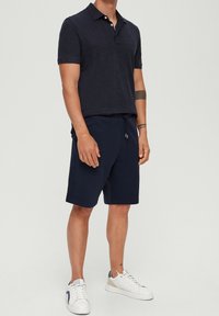 Polo bleu marine en tissu texturé, associé à un short assorti. Doté d'un col et d'une taille à cordon de serrage. Porté avec des baskets blanches.