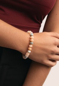 Pulsera de cuentas con colores pastel que incluyen rosa, azul y acentos dorados, con cuentas redondas dispuestas en un diseño flexible.