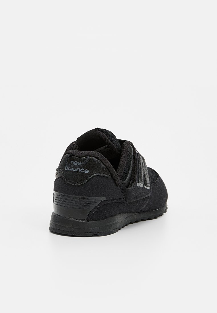 Chaussure de sport noire avec un dessus en daim, bout rond et semelle texturée. Présente un logo au niveau du talon et sur les côtés, conçue pour le confort.