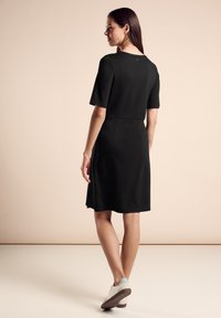 Zwarte jurk met korte mouwen, strakke lijfje en uitlopende rok. Gladde textuur, knie-lengte, gecombineerd met grijs-witte sneakers.