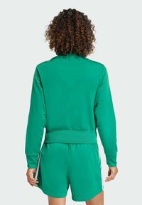 Zelená tepláková bunda s dlhými rukávmi, rebrovanými manžetami a zladeným pásom. Mäkká textúra látky, športový dizajn, bez viditeľných vzorov.