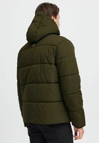 Jachetă puffer verde măsliniu cu glugă, având un design matlasat orizontal, textură pufoasă și un mic logo pe partea superioară a spatelui.