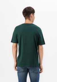Grøn bomulds T-shirt med rund hals, korte ærmer og en afslappet pasform, båret med blå jeans; ingen synlige grafikker eller mønstre.