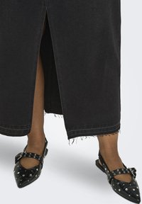 Zwarte denim maxirok met een midden-split en een rafelige zoom. Gecombineerd met zwarte platte schoenen met studs en een puntige neus.