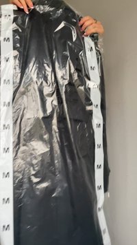 Haine negre într-un sac de plastic transparent, cu o bandă albă ce are inscripționat repetat litera "M" pe partea laterală. Materialul pare neted și ușor.