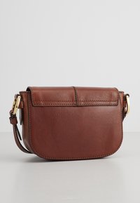 Borsa a tracolla in pelle marrone con forma arrotondata, chiusura a pattina, dettagli in metallo dorato e tracolla regolabile. Tessuto liscio, design minimalista.